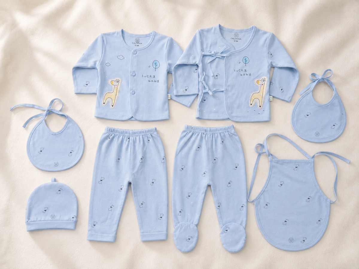 Les 7 pièces du coffret bleu posées à plat : 2 hauts, 2 pantalons, 2 bavoirs et 1 bonnet